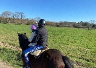 Adulto y niña montando juntos a caballo junto a un prado en la ruta a caballo de Gijón